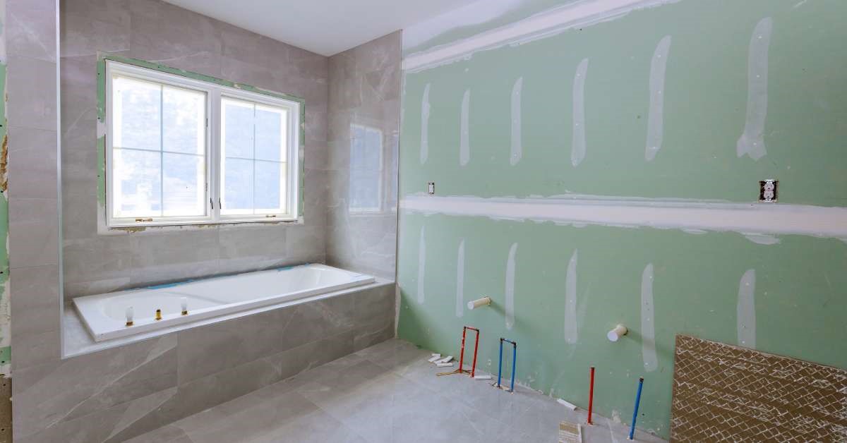 A residential home bathroom under construction. The waterproofed bath and sink plumbing are already installed.