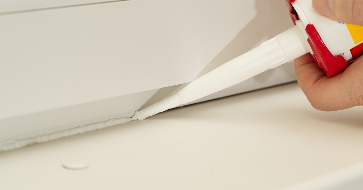 Silicone sealant flowing out of the nozzle of a bottle a in a person's hand onto the surface of a window to seal gaps.