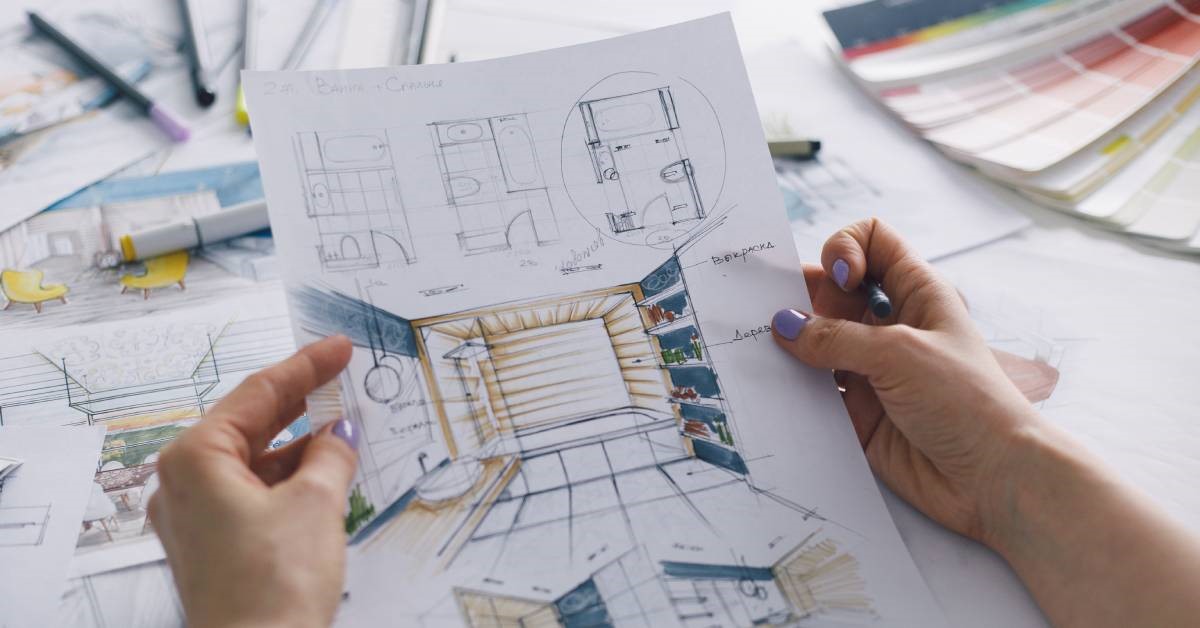 A woman’s hands holding a pen and custom bathroom design drawings for her upcoming remodeling project.