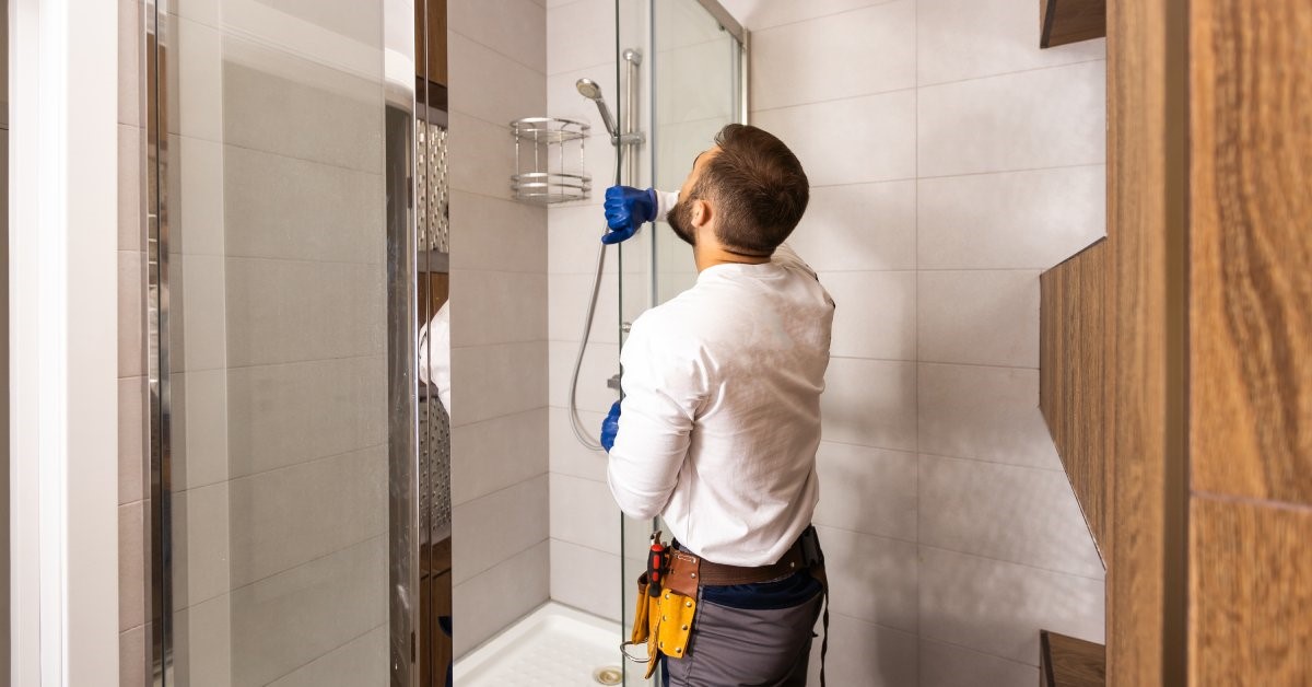 A professional contractor carefully installing a clear sliding glass door enclosure on a new shower.