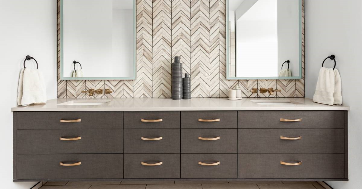 A luxury home bathroom featuring a double vanity with stone material countertops, a wooden backsplash, and large mirrors.