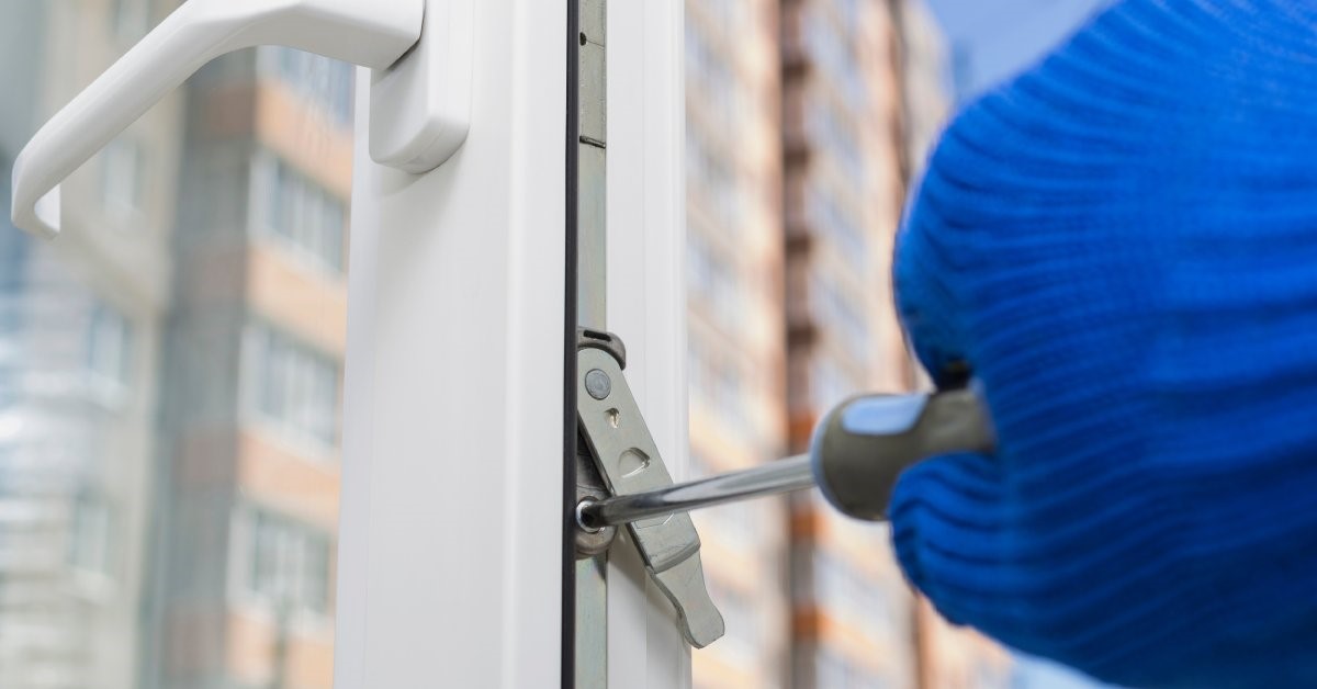 A close-up of a gloved hand using a screwdriver to adjust the security features on an open casement window.