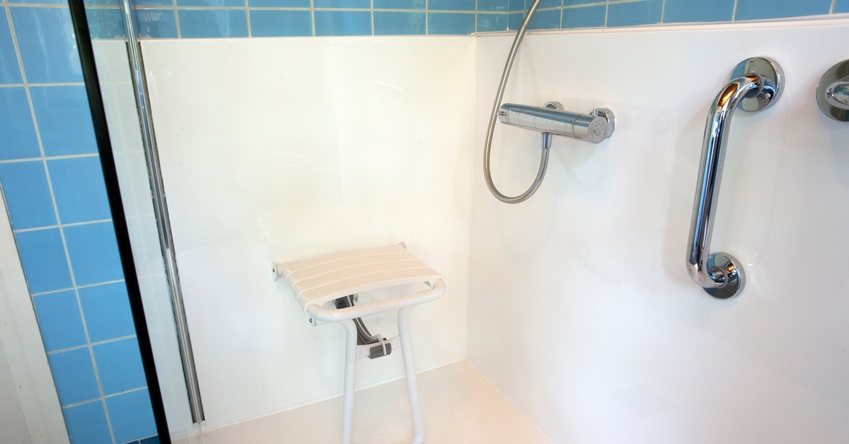 A silver grab bar installed on the wall in a bathroom. A person's hand grips the grab bar for support.