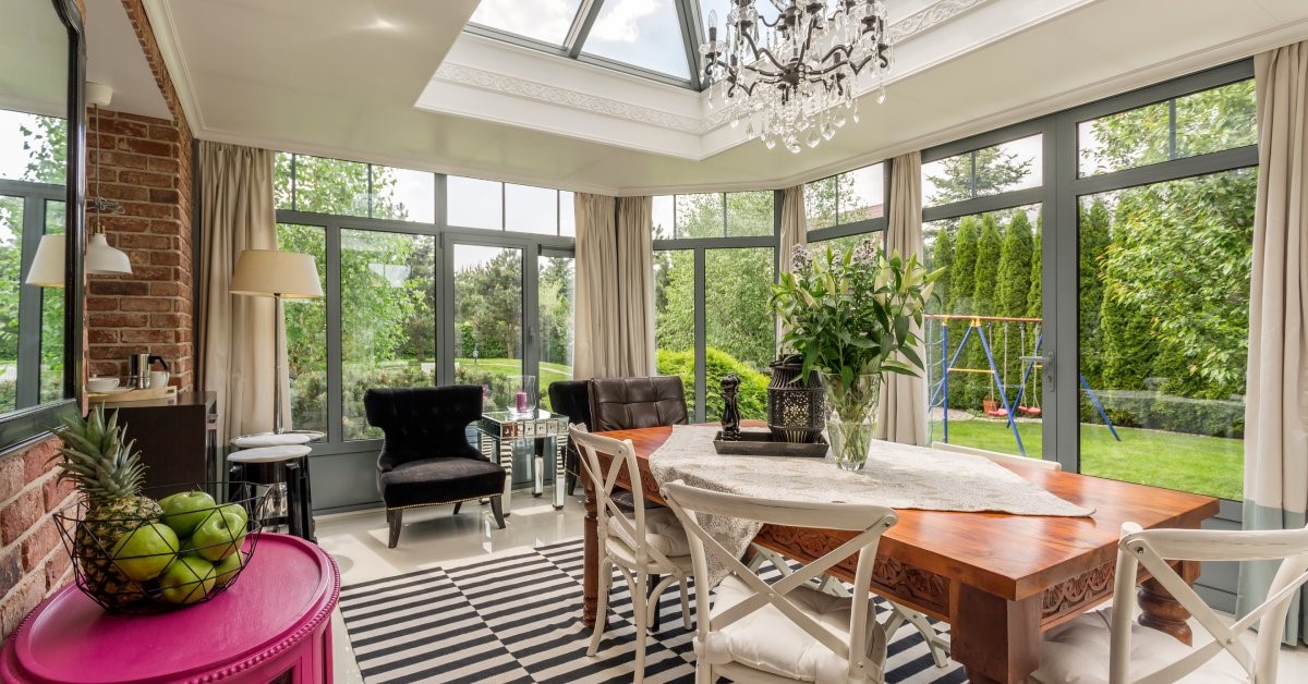 A spacious and modern residential sunroom, featuring large windows, window doors, and an expansive skyline.