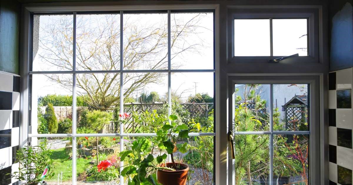 A garden kitchen window providing a sunny view of the backyard garden. The window features indoor plants and vibrant tiling.