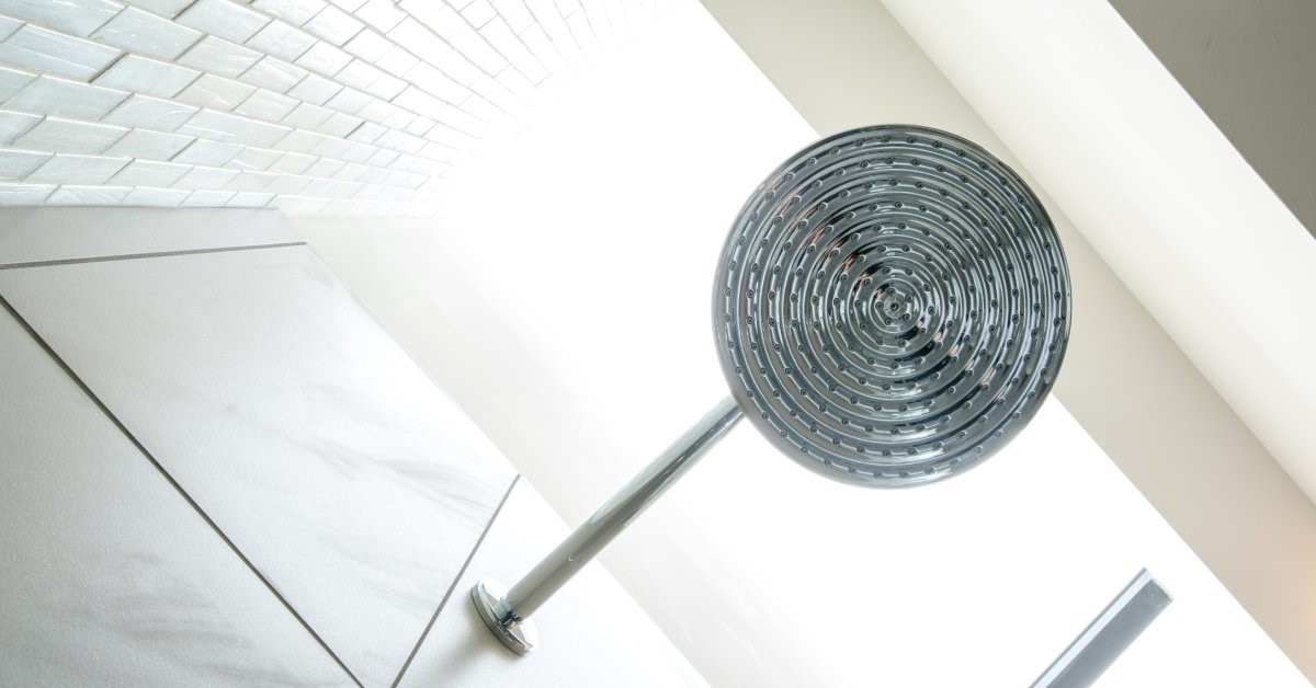 A close-up of a white-tiled shower with a combination rainfall-handheld showerhead mounted to the wall.