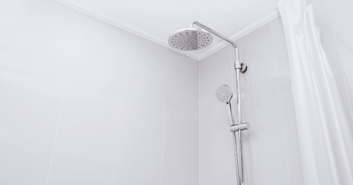 A close-up of a white-tiled shower with a combination rainfall-handheld showerhead mounted to the wall.