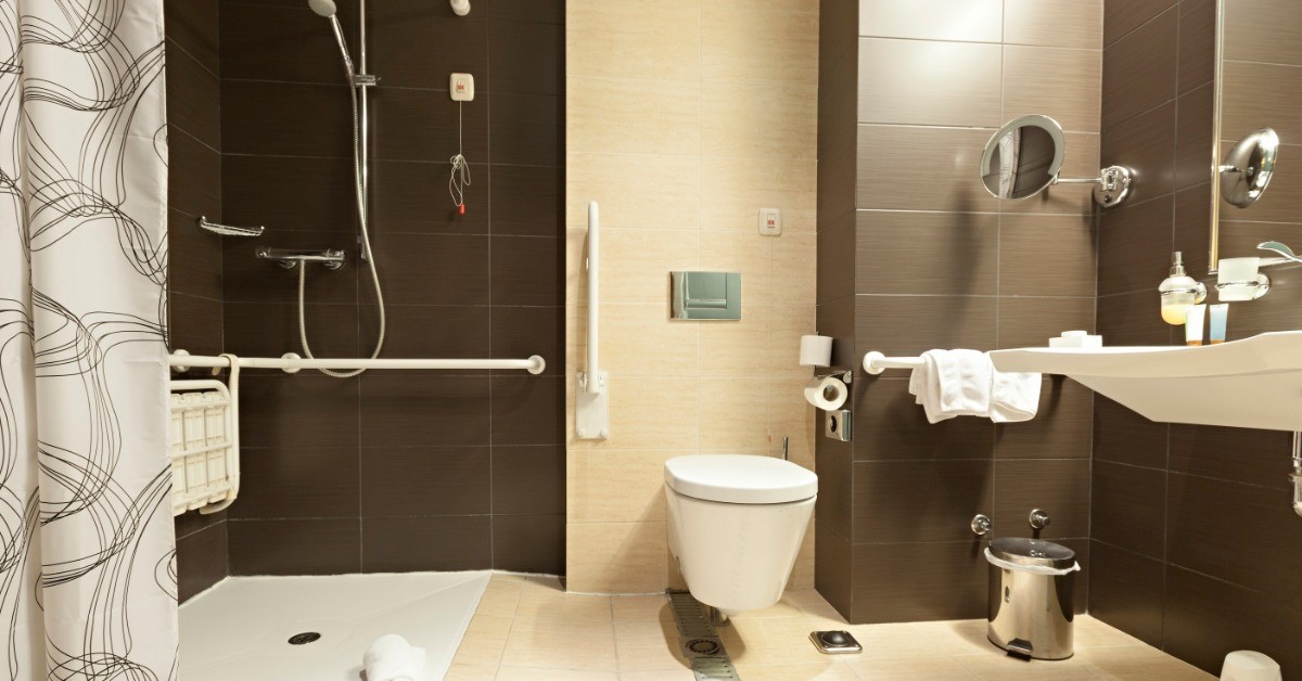 A roll-in shower is installed next to a toilet. There is also a small metal trash can next to the toilet.