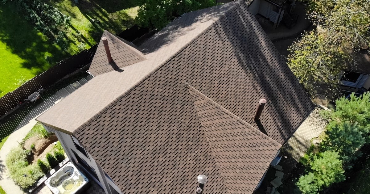 An aerial view of a home. There is a fence to the left of the frame and trees to the right of the frame.