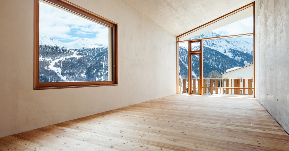 An empty room with a large window and a glass wall. Through the window there are mountains.