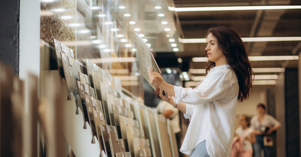 A woman is holding a piece of tile in her hands. She is wearing a white shirt and there are people in the background.