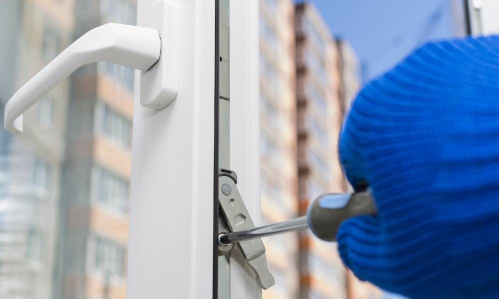 The hand of a window installer adjusts the encased locking system of a newly installed casement window with a screwdriver.