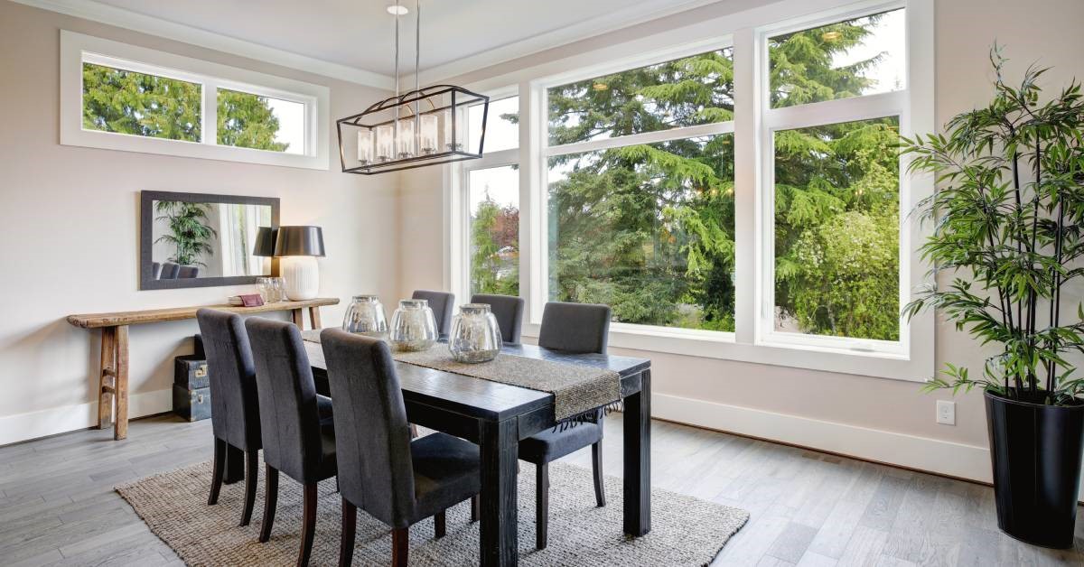 A modern and luxurious residential dining room with picture windows in the background, letting in lots of natural light.