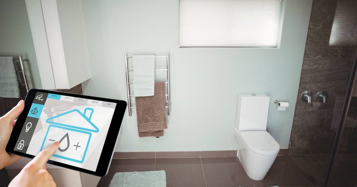 A person’s hands holding a tablet and using an application to adjust the settings on their smart toilet in their restroom.