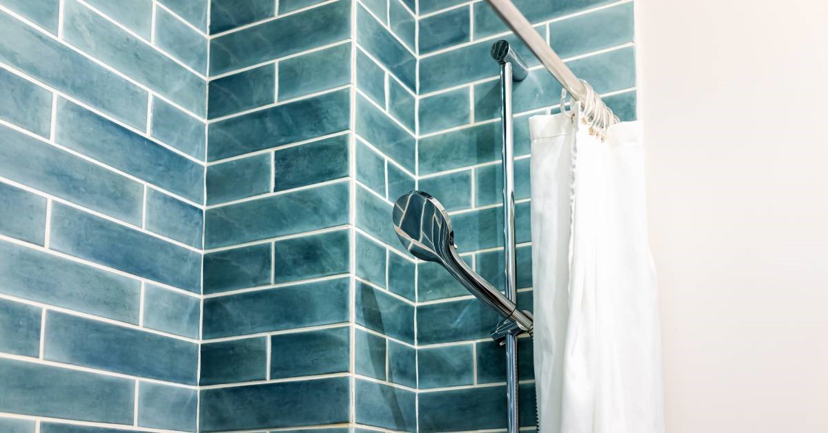 A modern bathroom shower featuring a white curtain, an adjustable shower head, and striking blue-green shower tiles.