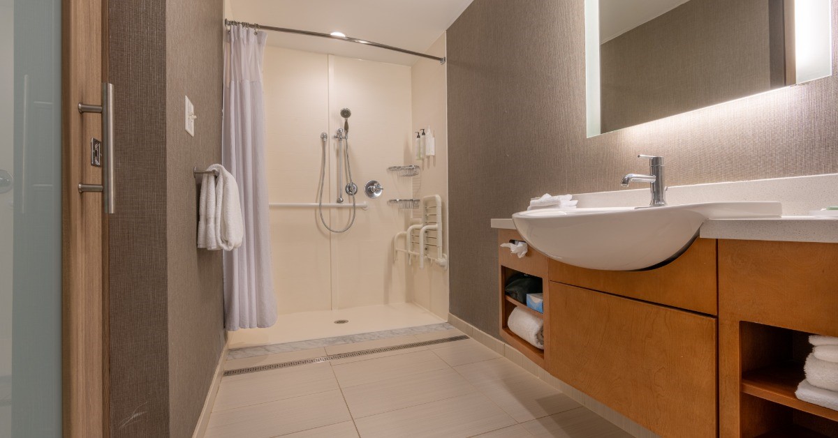 A bathroom that has a wheelchair-accessible shower to the left side of the frame. The curtain of the shower is pulled back.