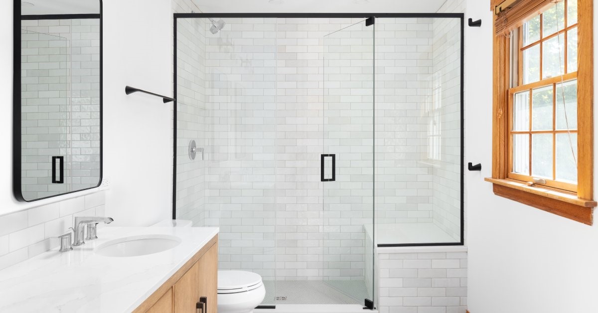 A white bathroom featuring updated hardware, including matte black metal trim around the mirror and shower door.