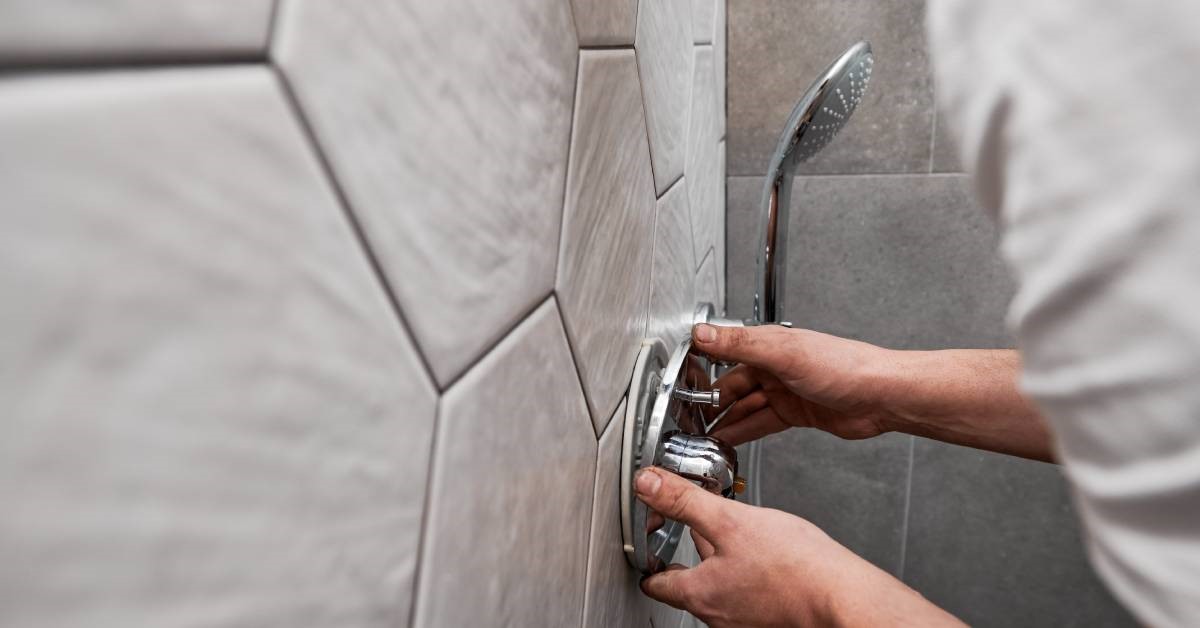 A man, up close, carefully installing a new and efficient shower faucet and handle into his renovated bathroom shower.