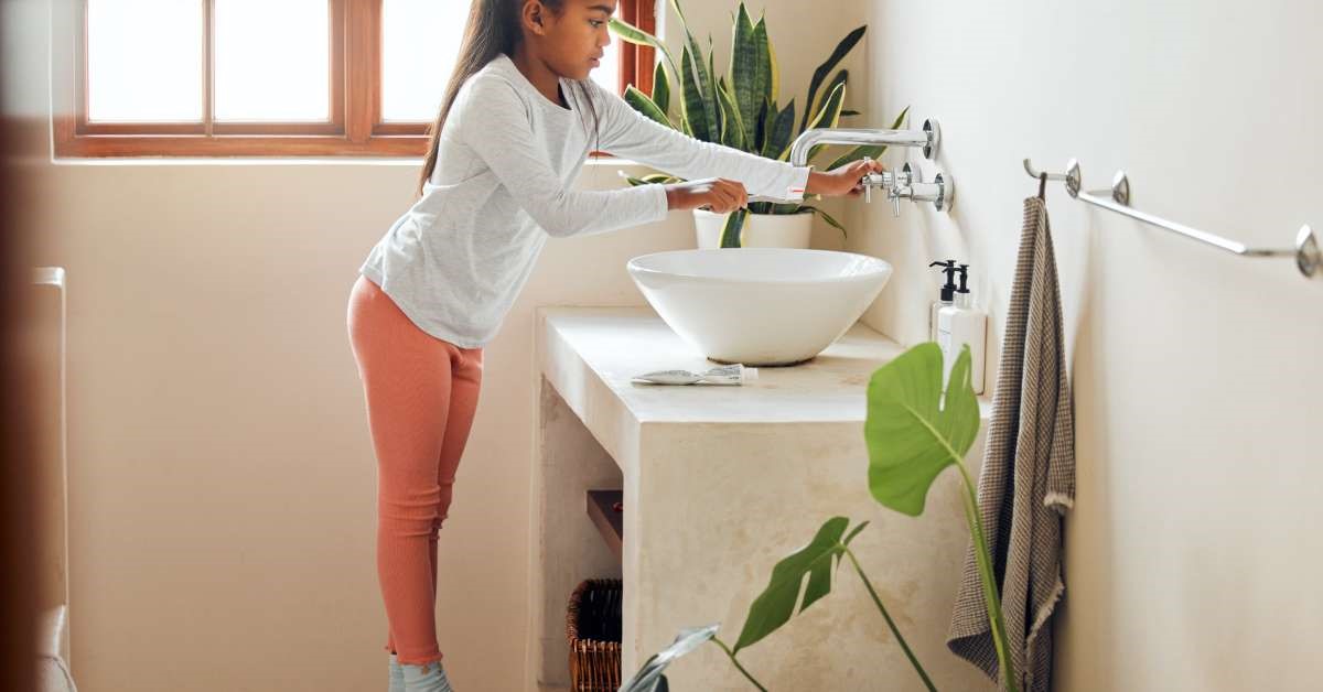 A child in a bathroom standing on a step stool to safely reach the sink for her morning dental care routine.