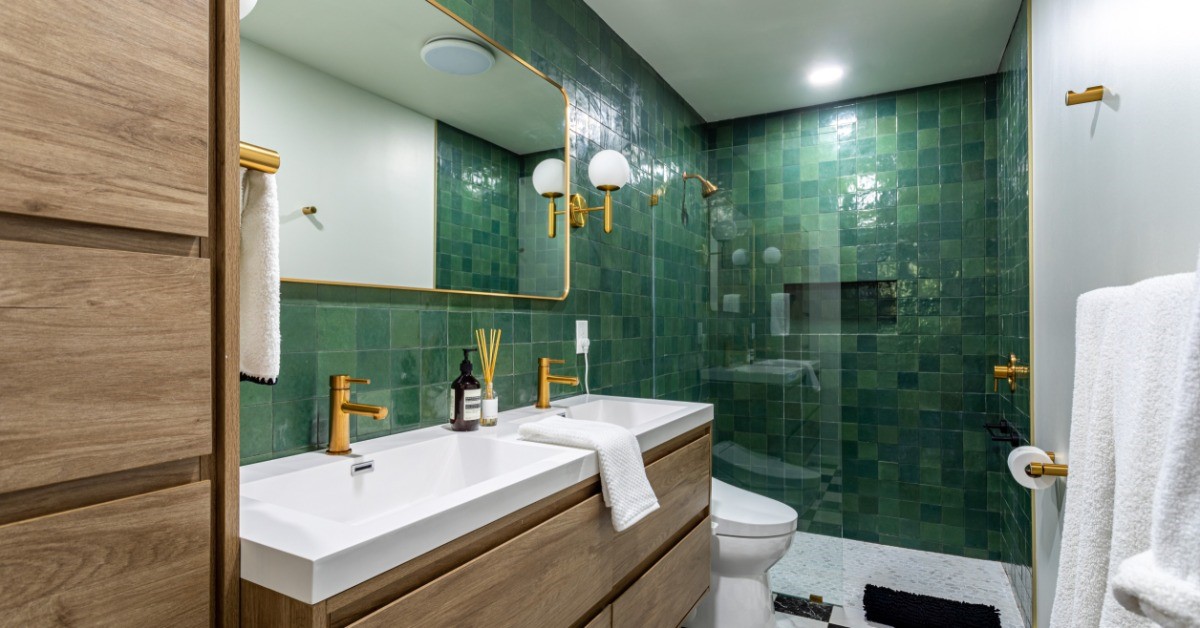 A bathroom has a black and white, checkerboard pattern tile on the floor and green tile installed in a shower.