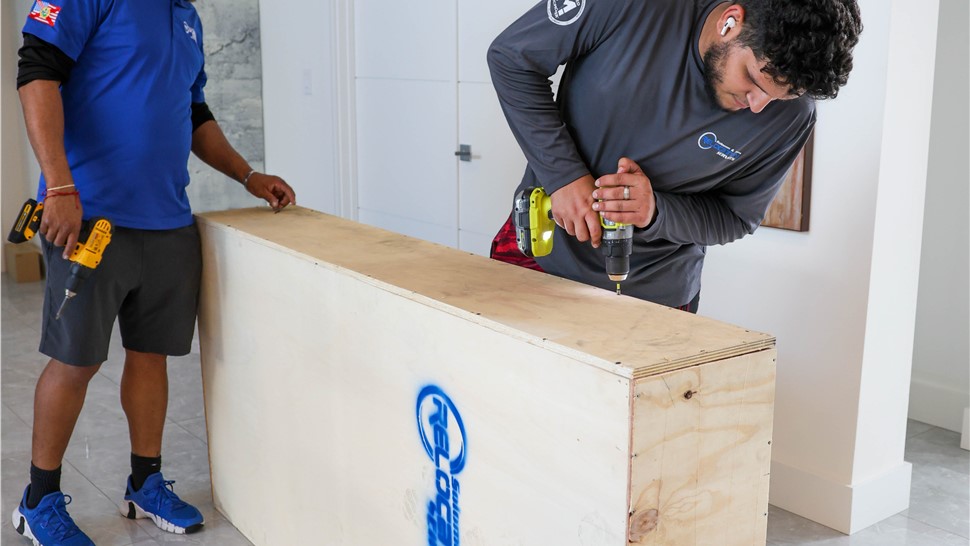 Two professional movers assembling a custom wooden crate indoors to protect large artwork during a residential move.