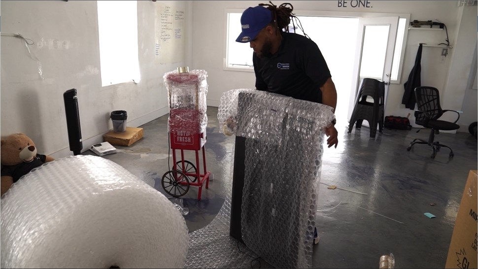 Mover bubble-wrapping large office equipment inside an office before loading for a commercial relocation.