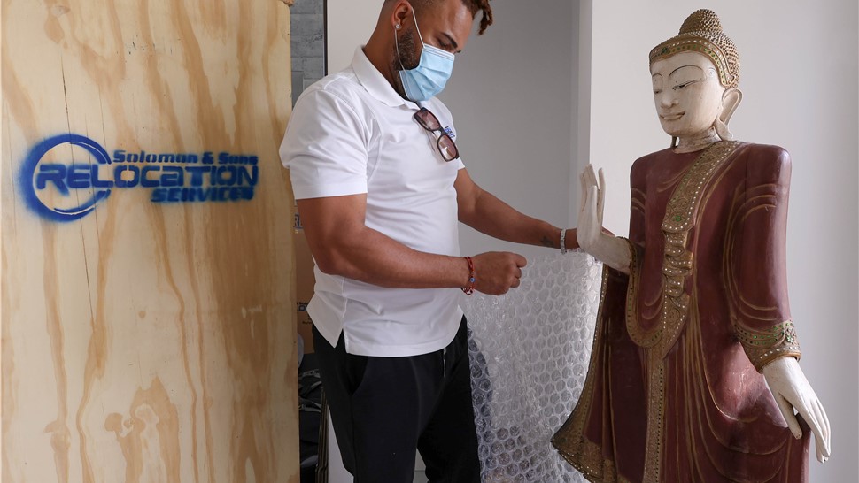 Mover inspecting a delicate statue next to a wooden moving crate inside a home.