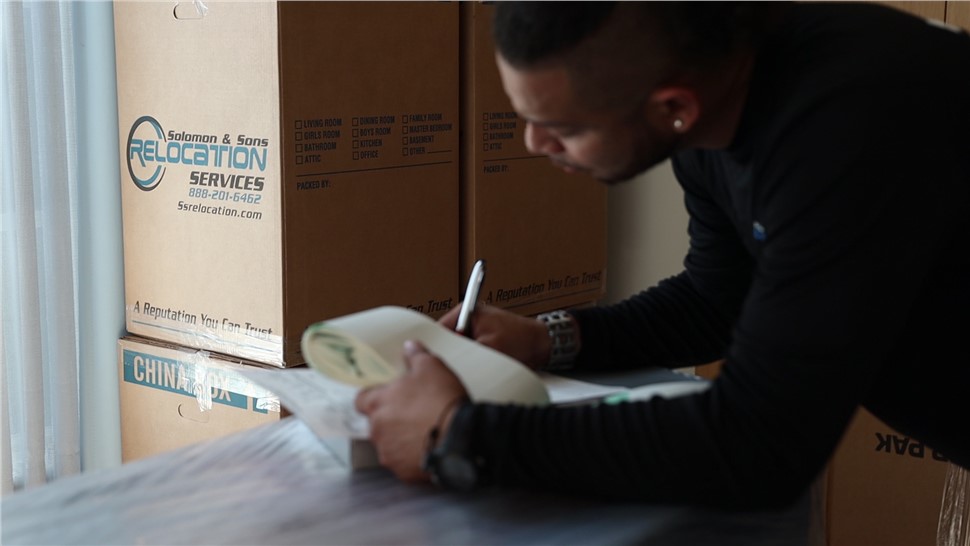 Team member writing inventory notes beside labeled moving boxes during an office relocation.