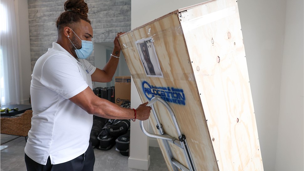 Mover securing a large wooden crate to a hand truck before loading.