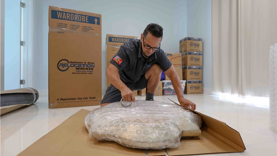 Mover bubble-wrapping a fragile wall piece with cardboard support for safe transport.