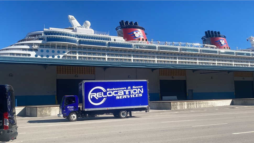 Blue Solomon & Sons Relocation Services box truck parked at a cruise port terminal with a large cruise ship behind it.