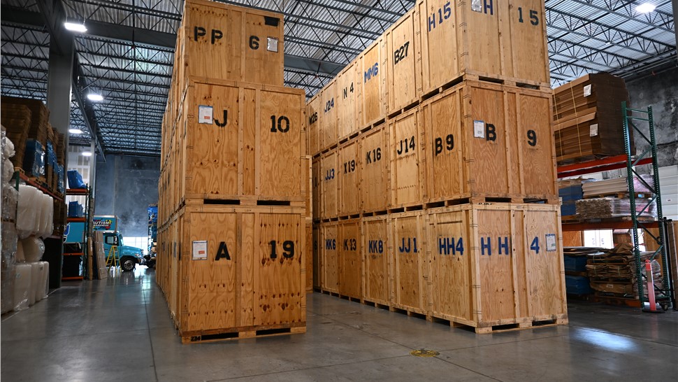 Tall stacks of wooden storage vaults and shipping crates on pallets inside a warehouse with high ceilings.