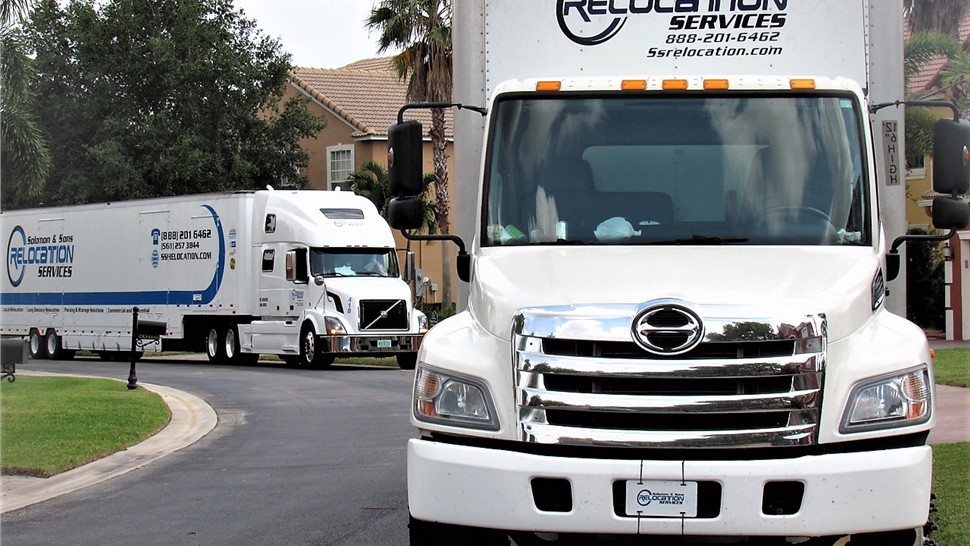 Solomon & Sons box truck with a branded tractor-trailer behind it in a residential neighborhood.