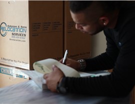 Team member writing inventory notes beside labeled moving boxes during an office relocation.