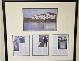 A framed article from 2004, titled "Against the Wind," detailing how The Roofing Company's work on the Pine Cone Harbor Condominiums successfully withstood Hurricane Isabel in 2003
