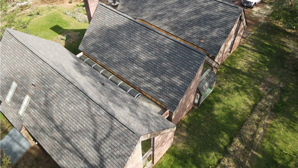 Angled aerial view of a complex luxury roof replacement in Virginia Beach, showcasing multiple steep roof facets with Royal Slate shingles and a custom curved skylight nestled in the flat valley.