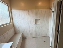 Walk-in shower conversion by Thompson Bath featuring marble-look wall panels, built-in shower niche, bench seating, and glass shower door in St. George, UT.