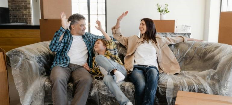 Family celebrating move while sitting on wrapped couch