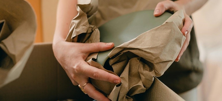 Hands carefully unwrapping dishes from packing paper, which is a good way to unpack efficiently in a small San Francisco apartment.