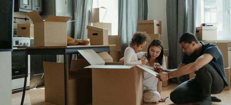Family who knows how to prepare your children for your move helping child decorate a moving box together