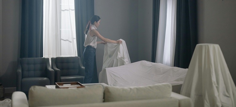 A person covers furniture to prevent damage, part of protecting your Bay Area home during a home relocation