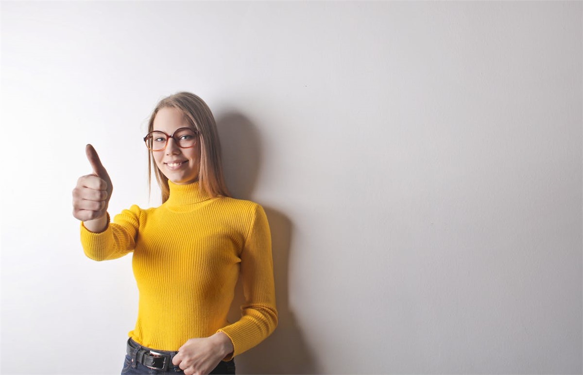 Woman in Yellow Turtleneck Sweater, Blue Denim Jeans, and Glasses Giving the Thumbs Up