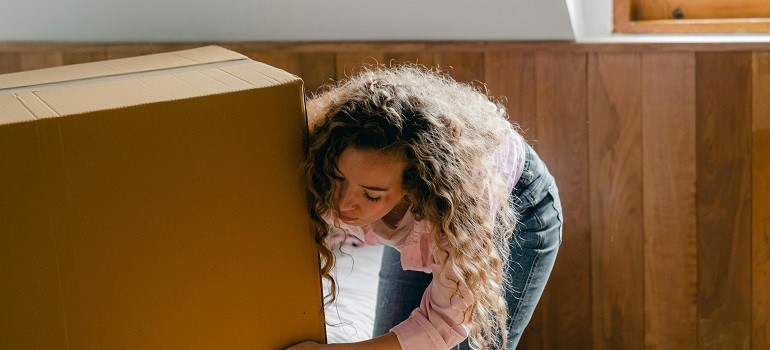 Woman lifting a large moving box inside apartment.