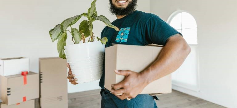 Person carrying moving box and houseplant indoors