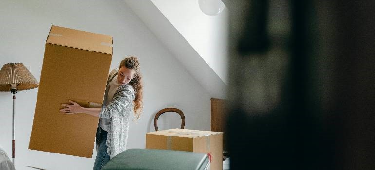 Woman lifting a large moving box upstairs at home