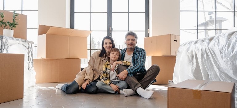 A family of three sits on the floor surrounded by cardboard boxes after moving with experts from full service moving services. 