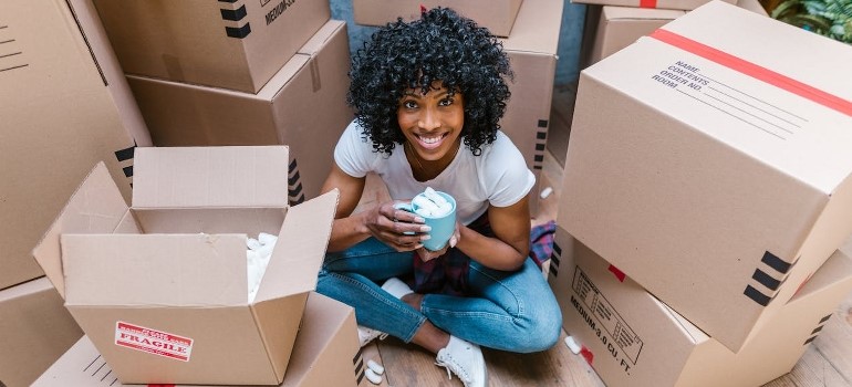 A woman is sitting on the floor, surrounded by moving boxes. 