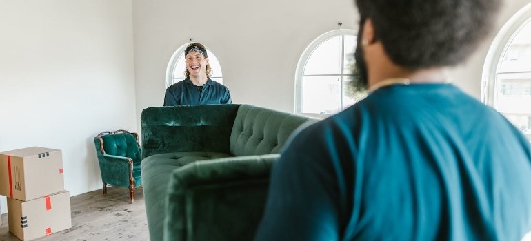 Two men carrying a green couch. 