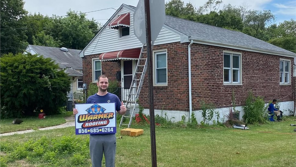 Homeowner standing near newly installed roof with Warner Exteriors sign