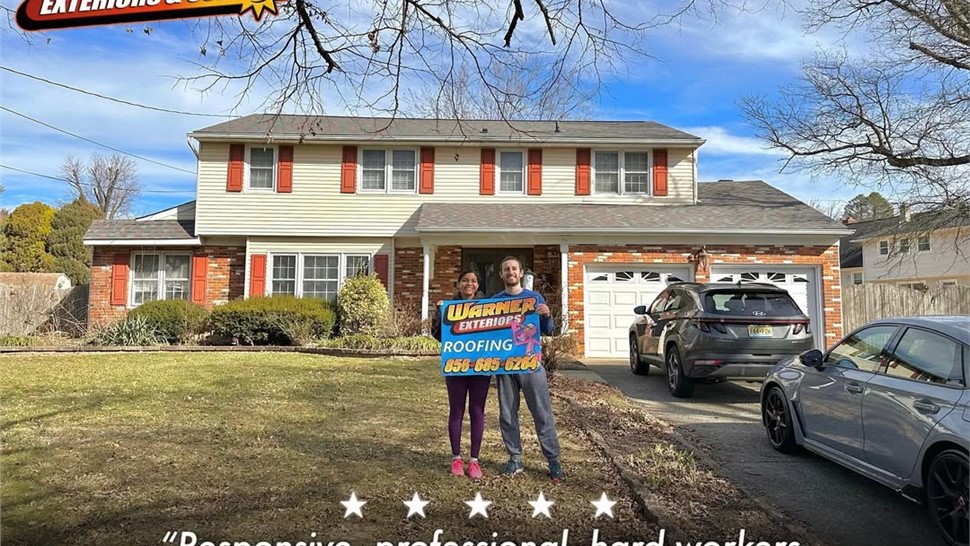 Homeowners holding Warner Exteriors roofing sign after completed roof installation.